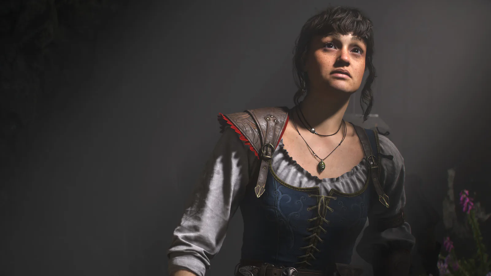 A young woman with short dark hair, a laced bodice and a leather shoulder guard looks upward